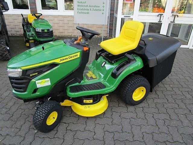 Der John Deere X147R Rasentraktor trägt das Baujahr 2021 und bringt ein Heckenauswurfmähwerk mit 92 cm Schnittbreite samt zwei Messern mit sich.